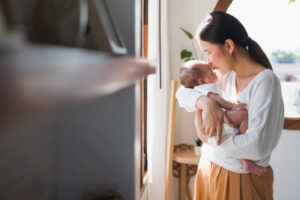 A young Asian American mother is holding her infant in her arms as she kisses their forehead.