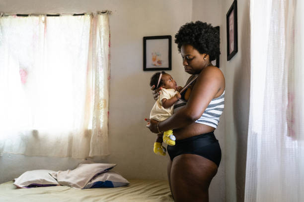 An African American mother is breastfeeding her baby girl in her bedroom.