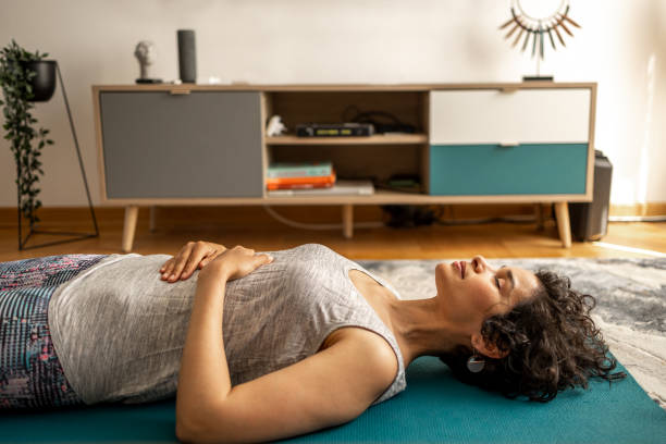 A young woman is laying on the floor on a yoga mat, meditating.