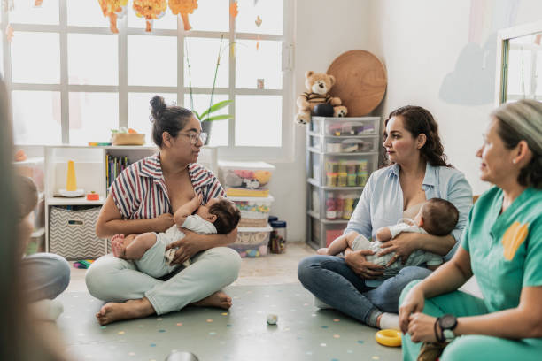 A group of women are taking part in a mother's support group, as they sit in a circle on the floor breastfeeding their babies.