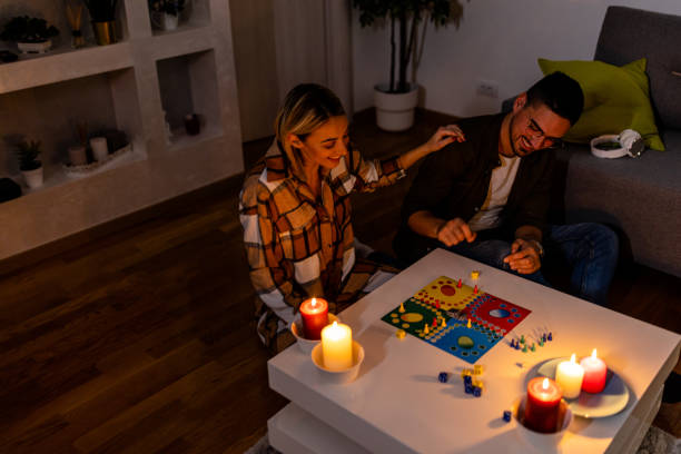 A young biracial couple is sitting on the floor of their living room playing a board game.