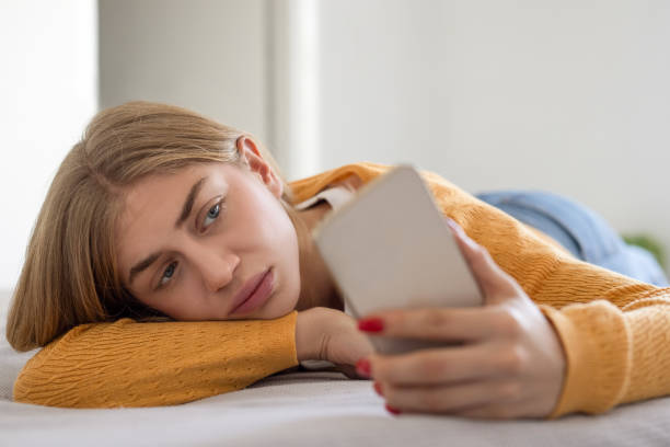 A young girl is laying down looking at her phone in her hand.