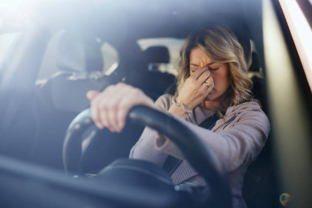 A woman sitting in the driver’s seat with one hand on the steering wheel and the other pinching the bridge of her nose, appearing stressed or overwhelmed.