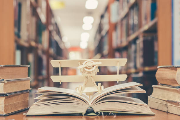 A book is open in a library, with a plane figurine on the open pages.