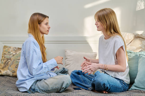 Two women sit cross-legged on a couch facing each other, engaged in a serious and focused conversation, suggesting a moment of open communication or emotional support.
