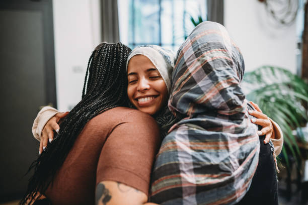 Three women share a warm group hug, with one smiling joyfully at the camera, symbolizing friendship, support, and a sense of belonging.