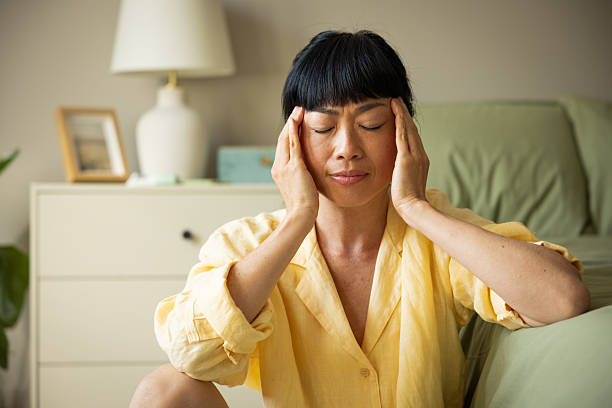 Mid adult woman waking up and having pains. She is sitting next to bed and having pain.