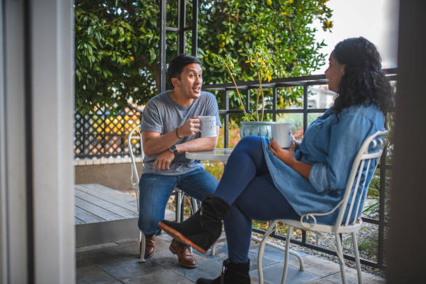 A couple sits on a patio, holding mugs and engaging in a lively conversation, suggesting open communication, emotional connection, and quality time in a healthy relationship.