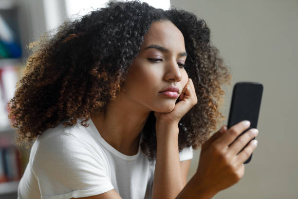A young woman rests her head on her hand while looking at her phone with a serious, concerned expression, suggesting worry, overthinking, or relationship anxiety triggered by digital communication.