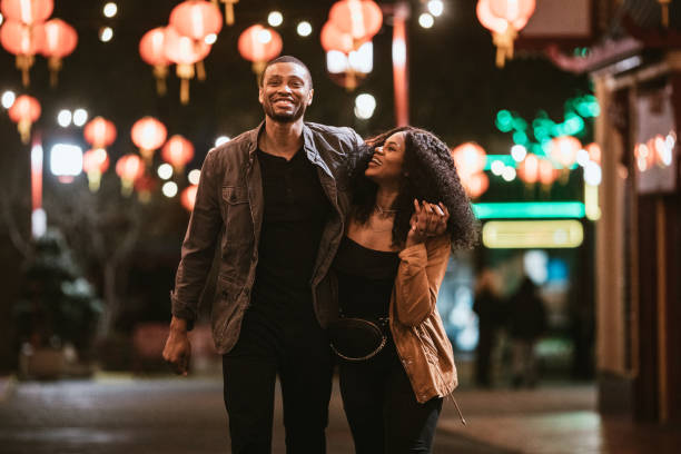 A smiling couple walks arm in arm under a canopy of glowing lanterns at night, sharing a joyful and affectionate moment that reflects emotional connection and relationship happiness.