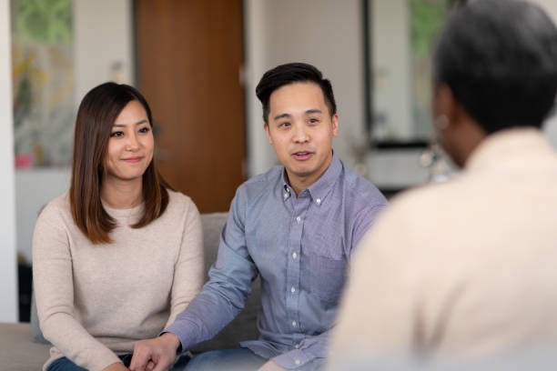 Asian couple sitting on a couch and talking to a therapist during a premarital counseling session, showing open communication and relationship support.