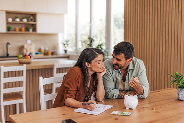 A couple sitting at a kitchen table with a piggy bank and financial papers in front of them, having a focused discussion about money and budgeting.