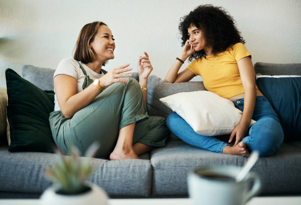 Two women sitting on a comfortable couch, engaged in a relaxed and meaningful conversation in a cozy living room setting.