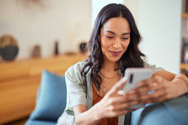Smiling woman sitting on a couch looking at her smartphone, appearing relaxed and engaged.