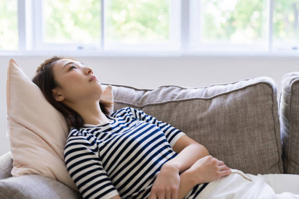 Woman lying on a sofa with hands resting on her stomach, gazing thoughtfully out the window.