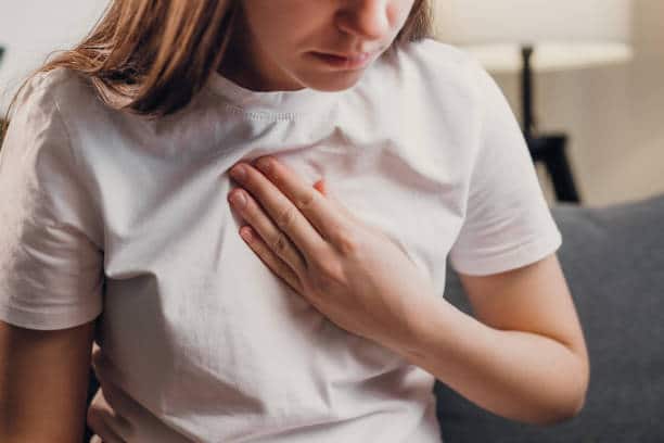 Woman holding her chest while experiencing anxiety symptoms, focusing on physical sensations in a moment of stress.