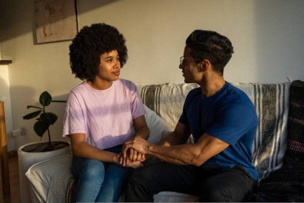 Couple sitting on a couch holding hands while having a calm and supportive conversation.