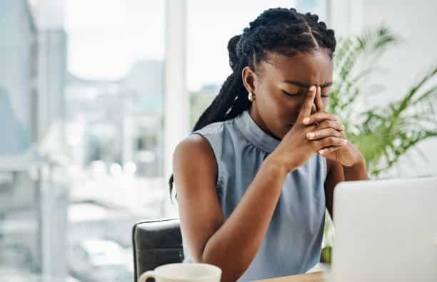 Woman sitting at a laptop with hands on her face, appearing anxious and mentally overwhelmed by perfectionistic thoughts.