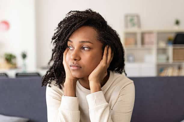 Woman sitting on a couch hugging herself while looking distressed, representing emotional struggle associated with OCD.