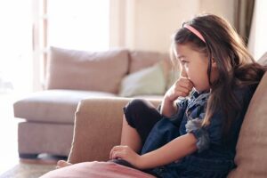 Young girl sitting on a couch biting her nails, showing a body-focused repetitive behavior like nail biting.