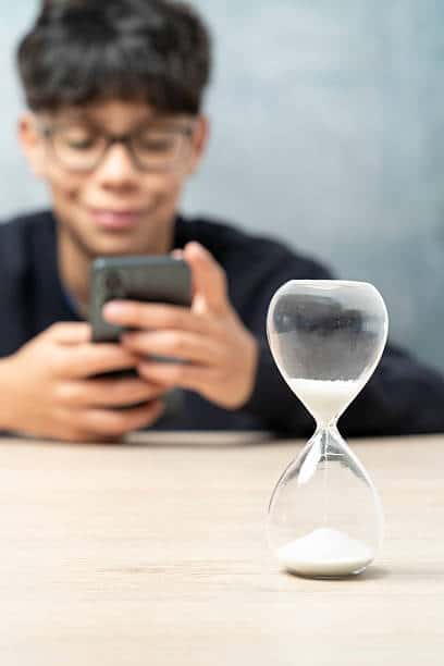 Student using a smartphone with an hourglass nearby, representing time management and screen-time challenges for children with ADHD.