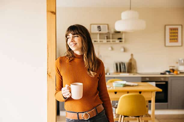 Woman standing in a cozy kitchen holding a coffee mug, looking out the window and enjoying a peaceful moment of reflection.