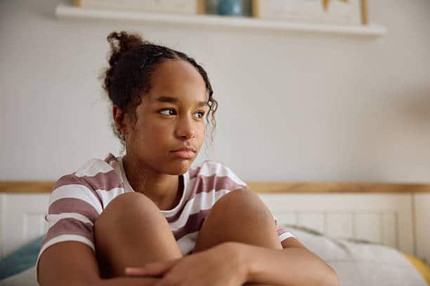 Depressed African American teenage girl thinking of her problems at home.