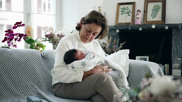 Elderly woman cradling newborn baby in cozy living room, warm and loving family moment, grandmother's nurturing embrace, intergenerational bonding, home interior